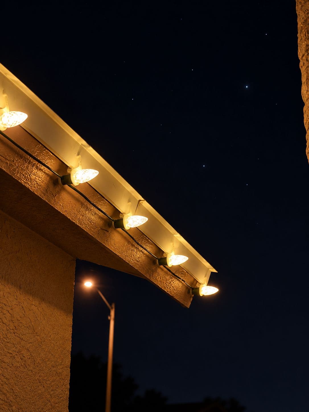 Close-up of warm white C9 bulbs clipped to a gutter edge against the night sky